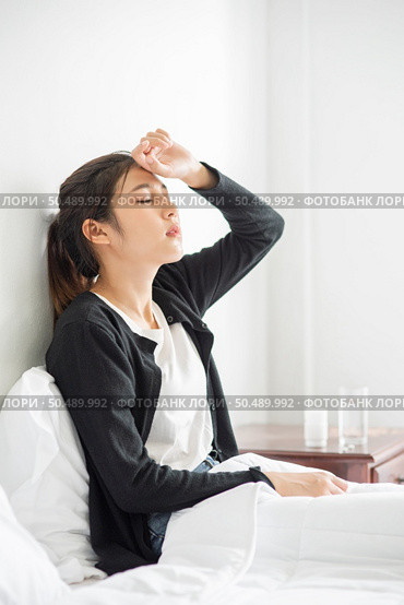 An uncomfortable woman sits on the bed and has medicine on the table. Стоковое фото, агентство Ingram Publishing / Фотобанк Лори