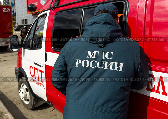 ANGARSK, IRKUTSK REGION, RUSSIA - April 08, 2025: On back of man in special clothing is inscription "EMERCOM of Russia" against background of red special equipment and fire trucks. Редакционное фото, фотограф Виктория Катьянова / Фотобанк Лори