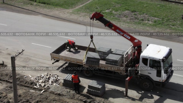 ANGARSK, IRKUTSK REGION, RUSSIA - May 18, 2023: Video of road workers in orange vests unloading pallets with curbs from a truck on the side of a road being repaired. Top view. Редакционное видео, видеограф Виктория Катьянова / Фотобанк Лори