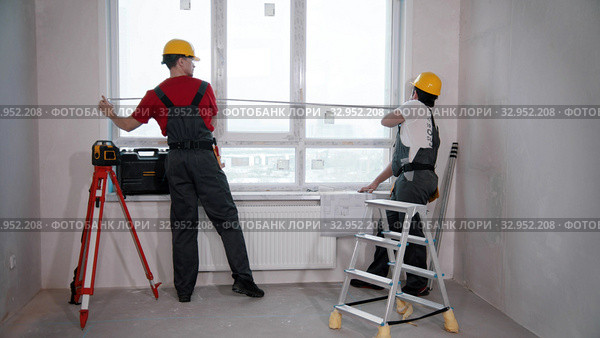 Apartment repair in the room - two men workers measuring the window. Стоковое фото, фотограф Константин Шишкин / Фотобанк Лори