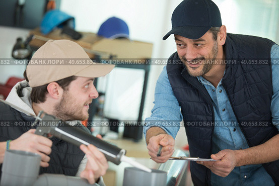 apprentice being advised how to apply caulk to window. Стоковое фото, агентство Ingram Publishing / Фотобанк Лори