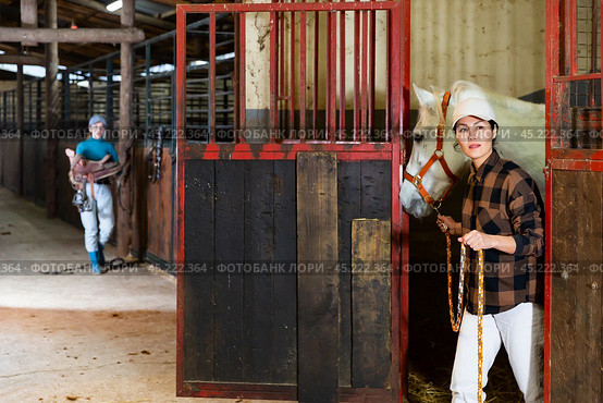 Asian female rancher leading white horse out of stall in stable. Стоковое фото, фотограф Яков Филимонов / Фотобанк Лори