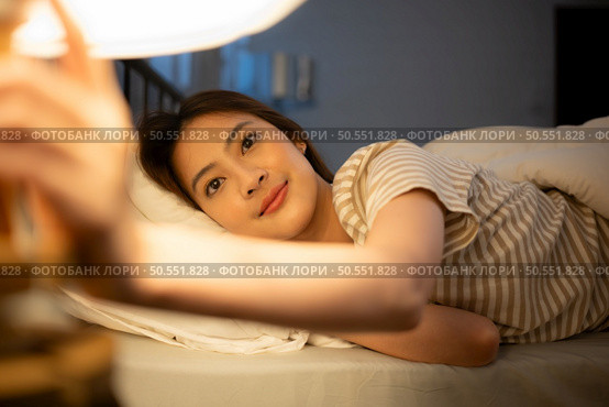 Asian woman lying on the bed turning off the light at the bedside to sleep tonight. Стоковое фото, агентство Ingram Publishing / Фотобанк Лори