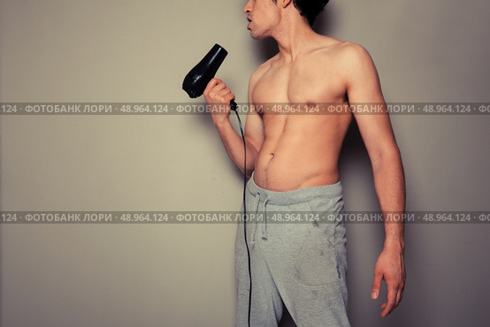 Athletic young man is holding a hair dryer and messing around with it. Стоковое фото, агентство Ingram Publishing / Фотобанк Лори