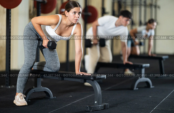 Athletic young woman pumping her biceps with a dumbbell while leaning on bench. Стоковое фото, фотограф Яков Филимонов / Фотобанк Лори
