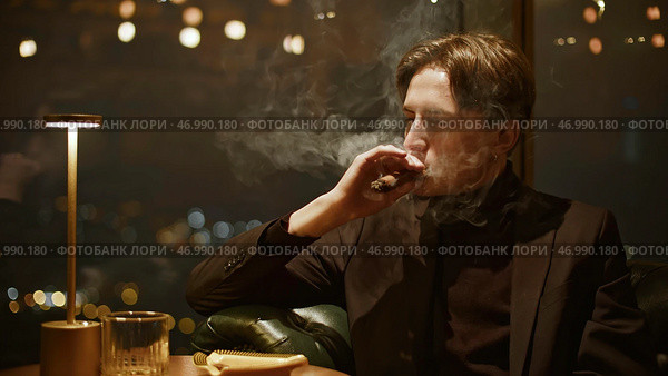 Attractive young man smokes cigar cinematically. Стоковое фото, фотограф David Kashakhi / Фотобанк Лори