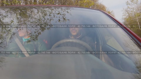 Автомобиль с мужчиной и женщиной отъезжает от обочины проселочной дороги. Мужчина за рулем. Вид через лобовое стекло. Дорога проходит через лес. Ветви деревьев и небо отражаются в стекле. Стоковое видео, видеограф Воловодов Владимир / Фотобанк Лори
