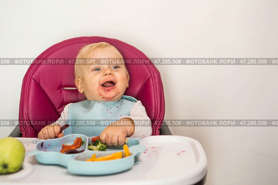 Baby food. The first meal. Feeding the baby. A cute little kid eats vegetables. Healthy food. The child is sitting on a high chair for feeding. Fresh vegetables and fruits. Стоковое фото, фотограф Photojuli / Фотобанк Лори