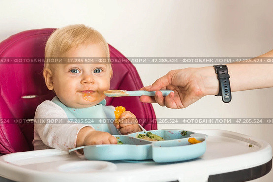 Baby food. The first meal. Feeding the baby. A cute little kid eats vegetables. Healthy food. The child is sitting on a high chair for feeding. Fresh vegetables and fruits. Стоковое фото, фотограф Photojuli / Фотобанк Лори