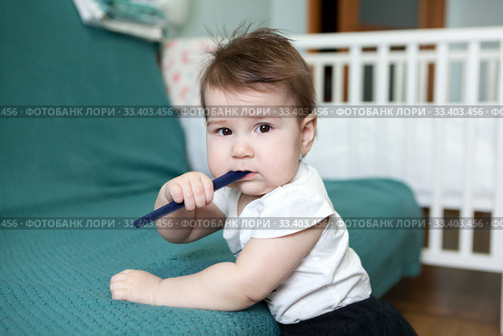Baby girl is chewing plastic hairbrush while teething, Caucasian child is in domestic room. Стоковое фото, фотограф Кекяляйнен Андрей / Фотобанк Лори