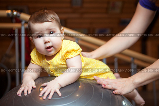 Baby girl lying on rubber fitball, mother doing exercises with her little daughter at home, holding the child body and ball. Стоковое фото, фотограф Кекяляйнен Андрей / Фотобанк Лори