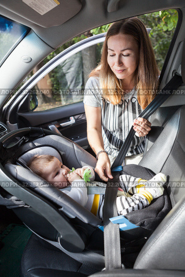 Baby in car seat for safety. Happy smiling mother placing baby in car seat and closing belt for safety. Стоковое фото, фотограф Кекяляйнен Андрей / Фотобанк Лори