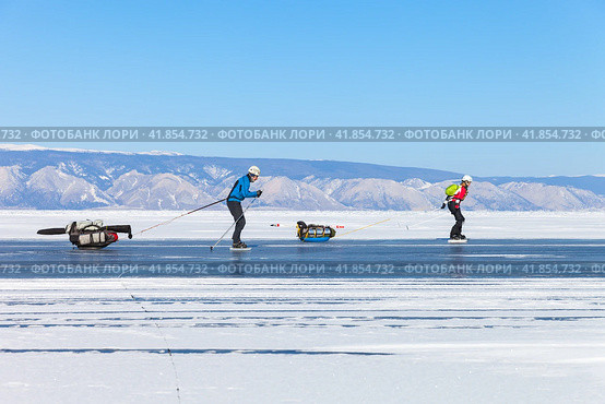 BAIKAL LAKE, IRKUTSK REGION, RUSSIA - February 22, 2015: Couple of tourists skate on ice of frozen Small Sea along Olkhon Island on frosty sunny day. Sleds carry tents, skis and overnight equipment. Редакционное фото, фотограф Виктория Катьянова / Фотобанк Лори