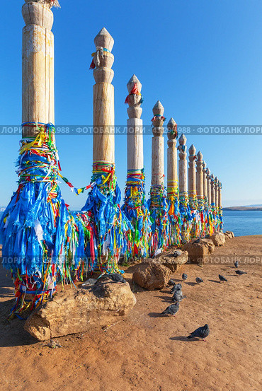 Baikal Lake. Olkhon Island. 13 Serge ritual pillars with blue and colored ribbons of Buddhists and tourists in Khuzhir village. Tourist attraction of Cape Burkhan. Pigeons are waiting for treats from tourists (2023 год). Стоковое фото, фотограф Виктория Катьянова / Фотобанк Лори