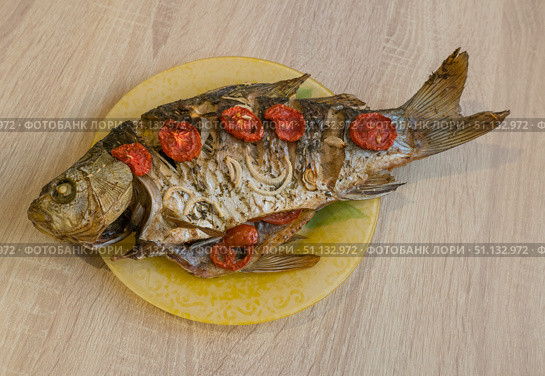 Baked large crucian fish with herbs, tomatoes and spices on a plate on the table. Стоковое фото, фотограф Екатерина Золина / Фотобанк Лори