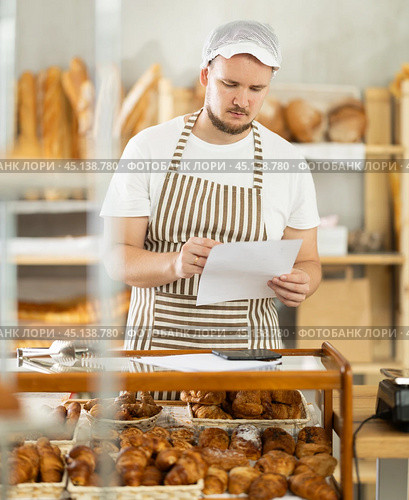 Bakery employee in apron examines documents, ponders debt restructuring. Стоковое фото, фотограф Яков Филимонов / Фотобанк Лори