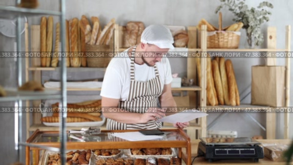 Bakery employee in apron examines documents, ponders debt restructuring. Стоковое видео, видеограф Яков Филимонов / Фотобанк Лори