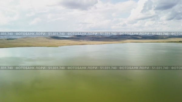 Bashkortostan, Russian Federation - August 07, 2025: Aerial view of tranquil lake reflecting clouds and mountains, showcasing serene landscape with lush greenery and open sky. Редакционное видео, видеограф Ирина Ручушкина / Фотобанк Лори
