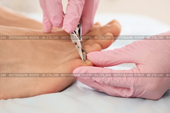 Beautician cutting cuticle off feet of young man on couch in spa salon, closeup. Стоковое фото, фотограф Pixel_shot / Фотобанк Лори