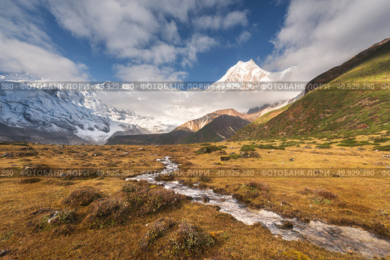 Beautiful landscape with high mountains with snow covered peaks, small river, yellow grass and cloudy sky at colorful sunrise. Mountain valley. Nepal. Amazing scene with Himalayan mountains. Nature. Mountains with snow covered peaks and small river. Стоковое фото, агентство Ingram Publishing / Фотобанк Лори