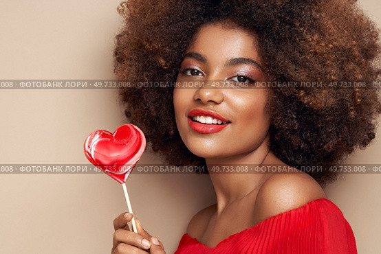 Beautiful portrait of an African girl with a heart shaped lollipop. Valentine’s Day. Symbol of love. Стоковое фото, агентство Ingram Publishing / Фотобанк Лори