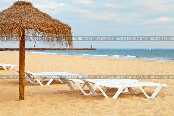 Beautiful sandy deserted beach with an umbrella and deck chairs on the sea shore. Natural sea background. Vilamoura Beach, Algarve, Portugal (2012 год). Стоковое фото, фотограф Виктория Катьянова / Фотобанк Лори