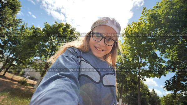Beautiful twelve-year-old teenager girl takes a selfie with a video camera on the background of sun rays and trees. Стоковое фото, фотограф Mikhail Davidovich / Фотобанк Лори