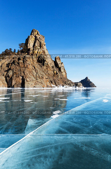 Beautiful winter landscape of frozen Baikal Lake on February. View from blue ice with cracks of famous rocks Big and Small Bell Towers (Kolokolny) - natural landmark and place of attraction for tourists. Стоковое фото, фотограф Виктория Катьянова / Фотобанк Лори