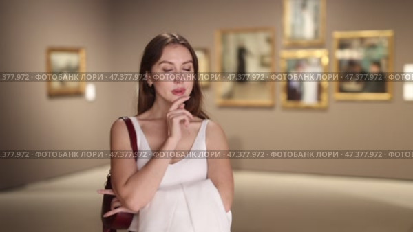 Beautiful woman in a gallery. European student visits a museum with interest and studies paintings and art. Стоковое видео, видеограф Яков Филимонов / Фотобанк Лори
