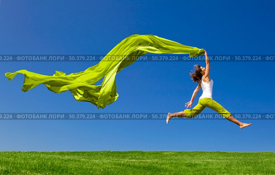 Beautiful young woman jumping on  a green meadow with a colored tissue. Стоковое фото, агентство Ingram Publishing / Фотобанк Лори