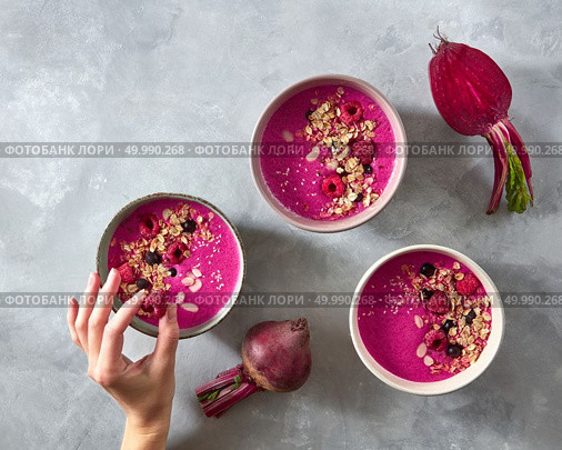 Beetroot smoothies with oatmeal and raspberry berries in a plate on a gray concrete background .The girl’s hand puts raspberries in a plate. The concept of a healthy diet. Top view. Three plates with a seafood smoothie with raspberries and oatmeal on a gray concrete frieze. A woman’s hand holds a berry. Top view. Стоковое фото, агентство Ingram Publishing / Фотобанк Лори