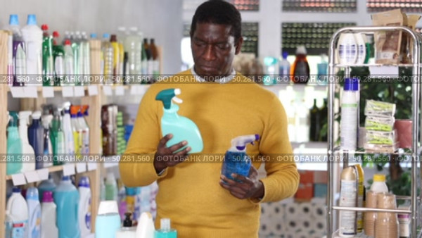 Before buying in household shop, African male customer choose glass cleaner spray. Стоковое видео, видеограф Яков Филимонов / Фотобанк Лори