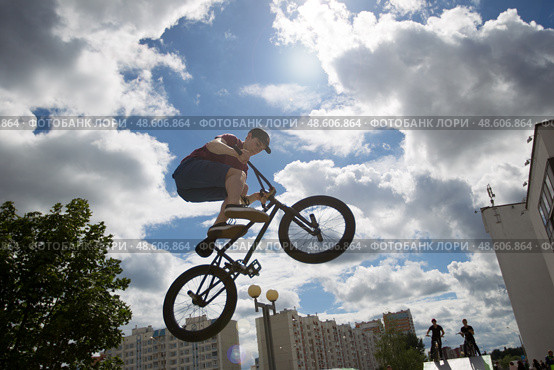 Belarus, Gomel, June 24, 2018. Central park. Extreme cycling.A dangerous trick on a bicycle against the backdrop of the city.A teenager on an extreme bicycle against the sky performs a jump. Редакционное фото, фотограф Лазаренко Светлана / Фотобанк Лори