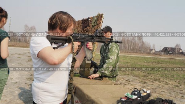 Berdsk, Russia, May 6, 2023. Weapon. An elderly woman picks up and takes aim from a Kalashnikov submachine gun with a collimator sight at a weapons exhibition. Hand held. Siberia. Редакционное видео, видеограф Сергей Медведев / Фотобанк Лори
