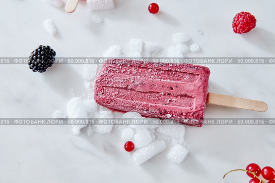 Berry apetitic organic ice cream lolly is represented on a gray marble table with different berries and ice cubes with a copy of the space. Ice cream on a blackberry stick with ice cubes, raspberry and red currant berries on a gray marble background with space for text. Healthy dessert. Flat lay. Стоковое фото, агентство Ingram Publishing / Фотобанк Лори