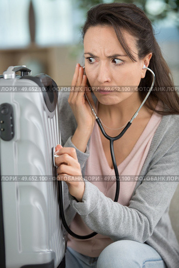 bewildered woman holding a stethoscope to her suitcase. Стоковое фото, агентство Ingram Publishing / Фотобанк Лори