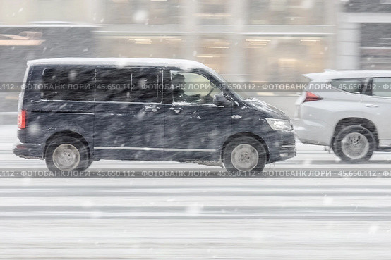 Black Volkswagen Multivan T6 riding at winter city street during snowfall. Редакционное фото, фотограф Константин Григорьев / Фотобанк Лори