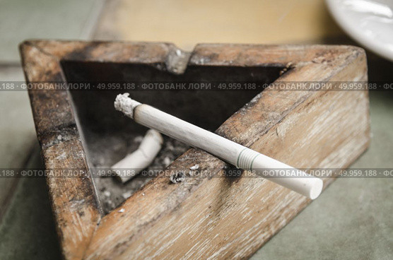 Black wood ashtray with cigarette stubs in closeup. Стоковое фото, агентство Ingram Publishing / Фотобанк Лори
