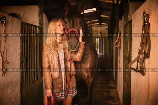 Blond girl holding horse at stable. Blond girl holding horse at stable corridor. Стоковое фото, агентство Ingram Publishing / Фотобанк Лори