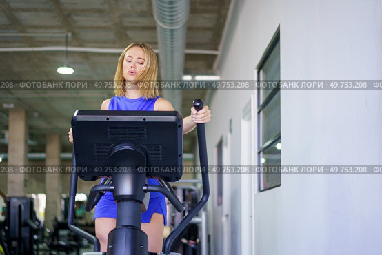 Blonde fit young caucasian woman exercising using elliptical machine in the gym. Woman exercising using elliptical machine in the gym. Стоковое фото, агентство Ingram Publishing / Фотобанк Лори