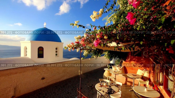 Blue church dome with wind playing with colorful flower shrub on a terrace of traditional cafeteria in typical greek village of Oia, Santorini island, Greece. Стоковое видео, видеограф Matej Kastelic / Фотобанк Лори