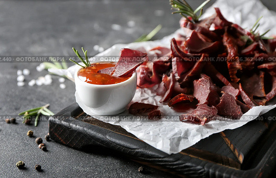 Board with spicy beef jerky and sauce on dark background. Стоковое фото, фотограф Pixel_shot / Фотобанк Лори