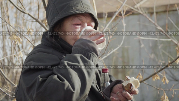 Бомж, бездомная женщина бродяга. Homeless unkempt woman in a temporary place drinks vodka, biting cheap food. Стоковое видео, видеограф EStarodubov / Фотобанк Лори