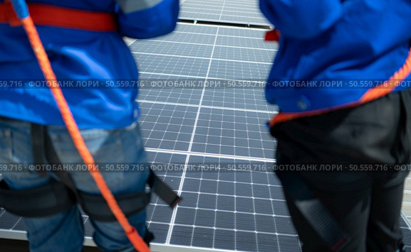 Both of technicians is installing solar panels on the roof of the warehouse to change solar energy into electrical energy for use in factories. Стоковое фото, агентство Ingram Publishing / Фотобанк Лори