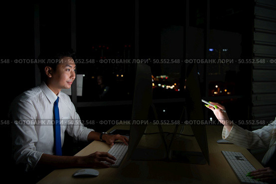 Both of young Asian broker international stock traders working together on desktop at night office, International financial investment company concept. Стоковое фото, агентство Ingram Publishing / Фотобанк Лори