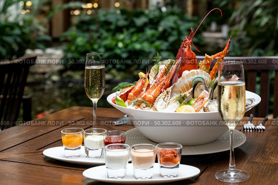 Bowl of gourmet fresh seafood on ice with savory sauce serve with white wine glass on vintage wooden table. Restaurant gastronomy food and drink consumerism concept. Стоковое фото, агентство Ingram Publishing / Фотобанк Лори