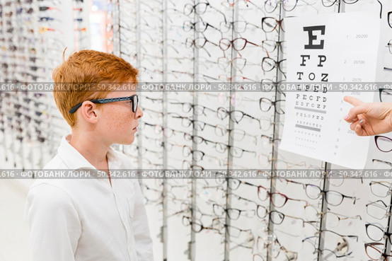 boy with spectacle looking snellen chart while doctor s hand pointing chart. Стоковое фото, агентство Ingram Publishing / Фотобанк Лори
