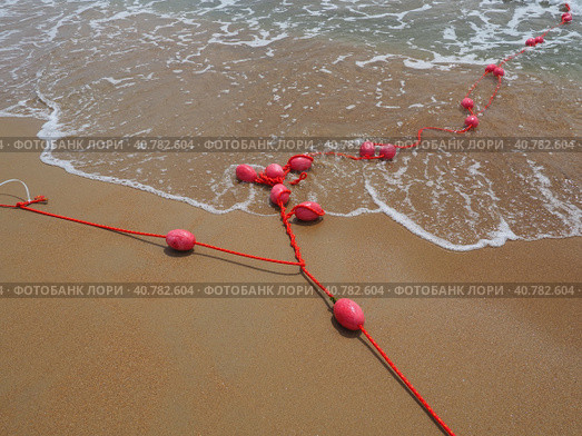 Buoys on a rope in sea water. The lifebuoys are pink restraints to alert people to the depth of the water. Rescue of the drowning. Delimiting a place on sandy beach between hotels. Wave with bubbles. Стоковое фото, фотограф Юлия Петровская / Фотобанк Лори