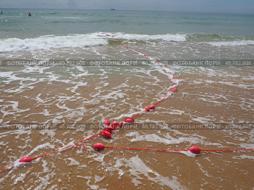 Buoys on a rope in sea water. The lifebuoys are pink restraints to alert people to the depth of the water. Rescue of the drowning. Delimiting a place on sandy beach between hotels. Wave with bubbles. Стоковое фото, фотограф Юлия Петровская / Фотобанк Лори