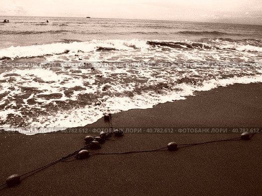 Buoys on a rope near sea water. The buoys are bright pink restraints to alert people to the depth of the water. Sepia. Delimiting a place on a sandy beach between hotels. Waves with bubbles. Стоковое фото, фотограф Юлия Петровская / Фотобанк Лори